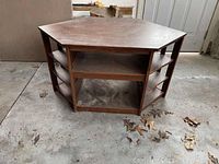 Front-facing photo of hexagonal oak corner media stand with multiple open shelves, dusty with visible dirt on top.