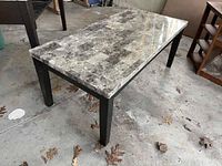 Coffee table with marble look top and black square legs on concrete floor showing surface details.
