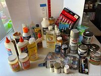 Full view of craft supplies including glues, solvents, spray paints, and various paint jars and bottles on a table.