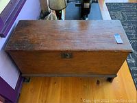 Top front view of vintage wooden blanket chest showing rectangular shape, hinged lid, metal latch, and surface wear.