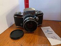 Front angled view of Exakta VX Ia camera with 50mm lens and lens cap placed beside it on a wooden surface.