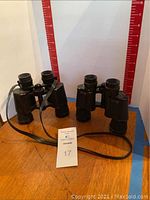 Front angle view showing two black 7x35 porro prism binoculars placed on a wooden surface with a blue and red measurement background.