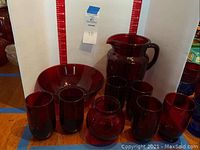 Front view of ruby red glassware set arranged showing pitcher, fruit bowl, and various glasses and vase.