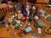 Wide angle of the dining table with full assortment of candles and holders laid out showing diversity of shapes, sizes, and colors.