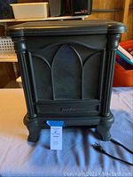 Overall view of the Duraflame electric fireplace heater showing decorative front with columns and four feet, power cord visible on surface.