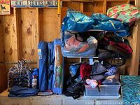 Full lot view showing shelving loaded with camping bags, tarps, and other accessories against wooden wall.