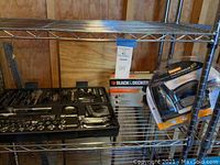 Shot of metal shelving with the tool set in a black molded case, Black & Decker sander box, and packaged electric stapler/nailer on shelf.