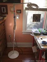 Full view of the white floor standing magnifying lamp with round base and adjustable arm set up in a room corner.