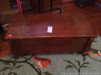 Closed view of the cedar chest showing wood grain and metal accent straps across the top and sides. Four legs visible at the base.