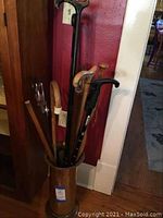 Photo showing several walking canes of different styles and handles standing inside a brass cane stand. The canes have various wood tones and one has a black handle with visible taped grip.