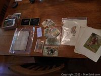 Wide view of assorted paper ephemera including cigarette cards, postcards, and illustrations laid out on a wooden surface.