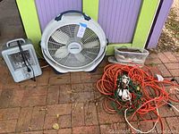 Image showing the entire lot with all items: box fan, heater, and cords on brick ground in front of colorful backdrop