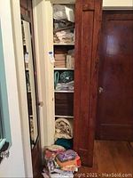 Closet shelf containing folded linens including towels, rugs, and tablecloths.