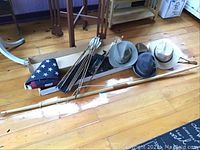 View of the bow, arrows, folded American flag, and assorted men's hats together on wooden floor.