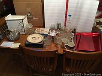 Wide view of lot items arranged on wooden table including Lenox box, salad plates, glassware, and chargers