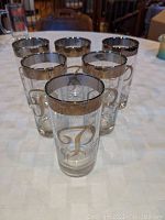 Set of six clear glass tumblers arranged in a cluster, showing silver band rim and monogrammed 'P'.