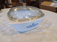 Side angled view of Corning Ware Dutch Oven showing blue cornflower pattern and clear glass lid with metal handle.