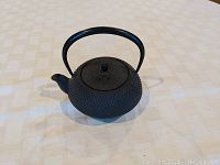 Full side view of the small cast iron hobnail teapot showing the rounded body, spout, lid, and bail handle.