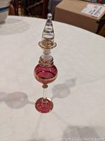 Full view of slim amethyst blown glass perfume bottle with clear stopper and gilt banding on bulbous body, neck, and base.