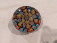 Top angled view of the round millefiori glass paperweight showing internal colorful floral pattern and shine on clear glass surface.