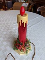 Front view of the vintage electric candle showing the red body, yellow top, and greenery base.