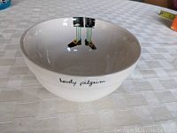 White ceramic bowl shown on a checkered tablecloth. Interior shows pilgrim legs design near the rim.