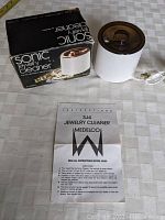 Medelco SJ4 Sonic Jewelry Cleaner, original packaging box, and power cord visible on a table surface.