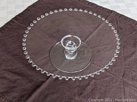 Top view of clear glass cake stand showing beaded edge and single ball stem base on brown cloth.
