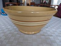 Side view of large yellowware bowl showing brown and white horizontal stripes on exterior, wide flared rim, rounded base.