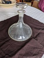 Full shot of clear glass decanter with stopper, displaying shape and overall look.