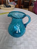 Front view of the blue glass pitcher with elegant twisted pattern and handle on a checkered tablecloth.