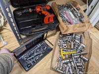 Overall view of drill case with cordless drill and two boxes filled with assorted wrenches and sockets.