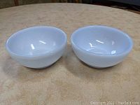 Two Fire King Blue Azurite chili bowls side by side on a beige surface, showing round shape and blue translucent glaze.