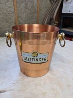 Front side of copper champagne bucket showing Taittinger logo and bronze handle mounts
