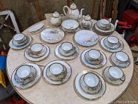 Overall view of the 42 piece Kutani style Japanese porcelain tea set arranged on a round table, showing cups, saucers, plates, teapot, creamer, sugar bowl, waste bowl, two large plates, and oblong ruffled dish.