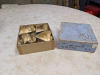 Top view of four tin cookie cutters arranged on a table next to original gold-toned box.