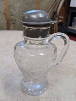 Front view of glass pitcher showing embossed strawberry pattern and nickel plated tin lid with hinge and latch mechanism.