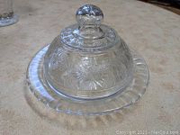 Strawberry butter dish full view showing glass plate and domed cover with knob handle. Item placed on a beige surface.