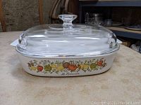 Side view of the casserole dish showing the colorful vegetable pattern and Le Romarin label