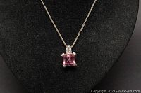 Front view of the necklace showing the pink square gemstone pendant with clear accent stones on a rope-style chain against a black background.