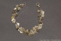 Bracelet laid flat on a solid colored background showing chain and multiple square dangling charms.