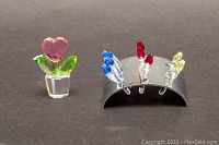 Photo displaying the pink heart-shaped flower figurine with two green leaves next to the metal display stand holding 3 red tulips, 3 blue tulips, and 2 yellow tulips.