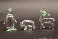 Full frontal photo of three Swarovski crystal figurines against gray background: faceted penguin, bear, and moose, all with green tape on some parts and visible chips or missing pieces.