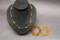 Front view of amber nugget necklace on black display bust with two amber nugget bracelets placed in front on black background.