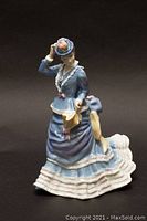 Front and angled view of Royal Doulton Lady Eaton figurine in blue dress holding a yellow fan, showing detailing and paint work.