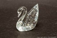 Small clear crystal swan figurine shown from front angle on a dark background, showcasing bubble detail inside the body.