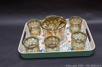 Full set of glassware on tray showing one ice bucket with tongs and six cocktail tumblers with gold overlay.
