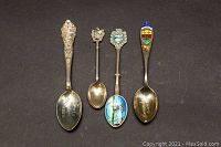 Four sterling silver collectible spoons arranged on black background, showing fronts with various designs, including engraved 'FREEDOM' spoon and colored enamel accents.