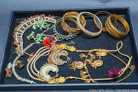 Photo of overall assortment of East Asian style costume jewelry including necklaces, earrings, and bangles laid out in a black tray