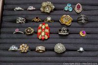 Top view of 20 assorted costume rings displayed in a jewelry tray showing various stone colors and floral designs.